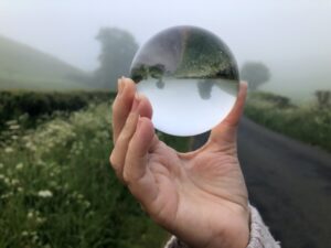 crystal lens ball in a woman’s hand, with a refracted view of a misty country lane