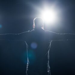 Man in black clothes standing with outstretched arms in bright light
