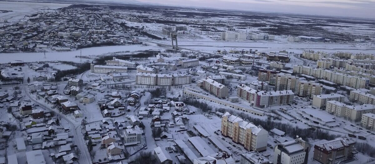 Aerial view of a big city with building roofs covered by snow. Clip. Flying above frozen city and a