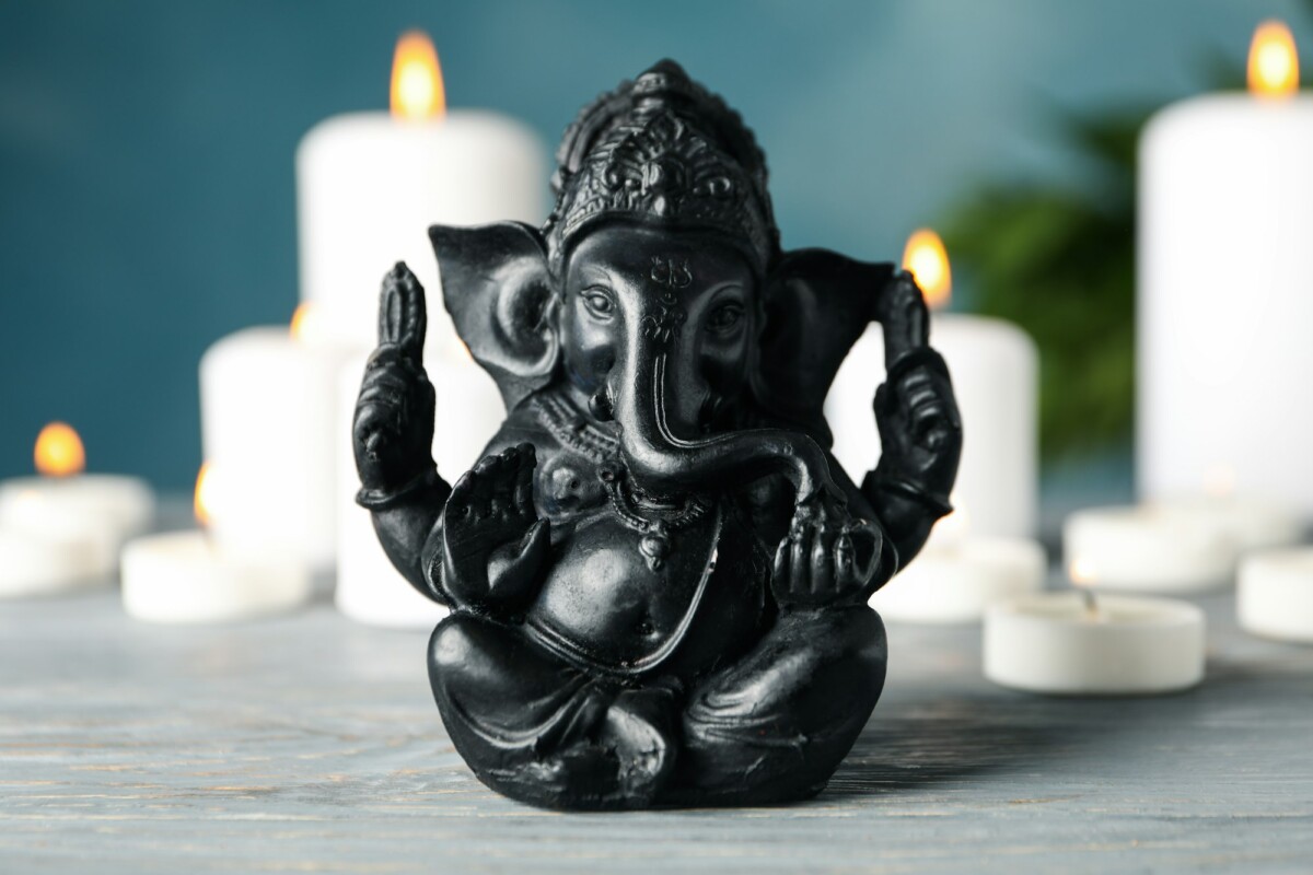 Hindu god Ganesha on white wooden table. Candles on background